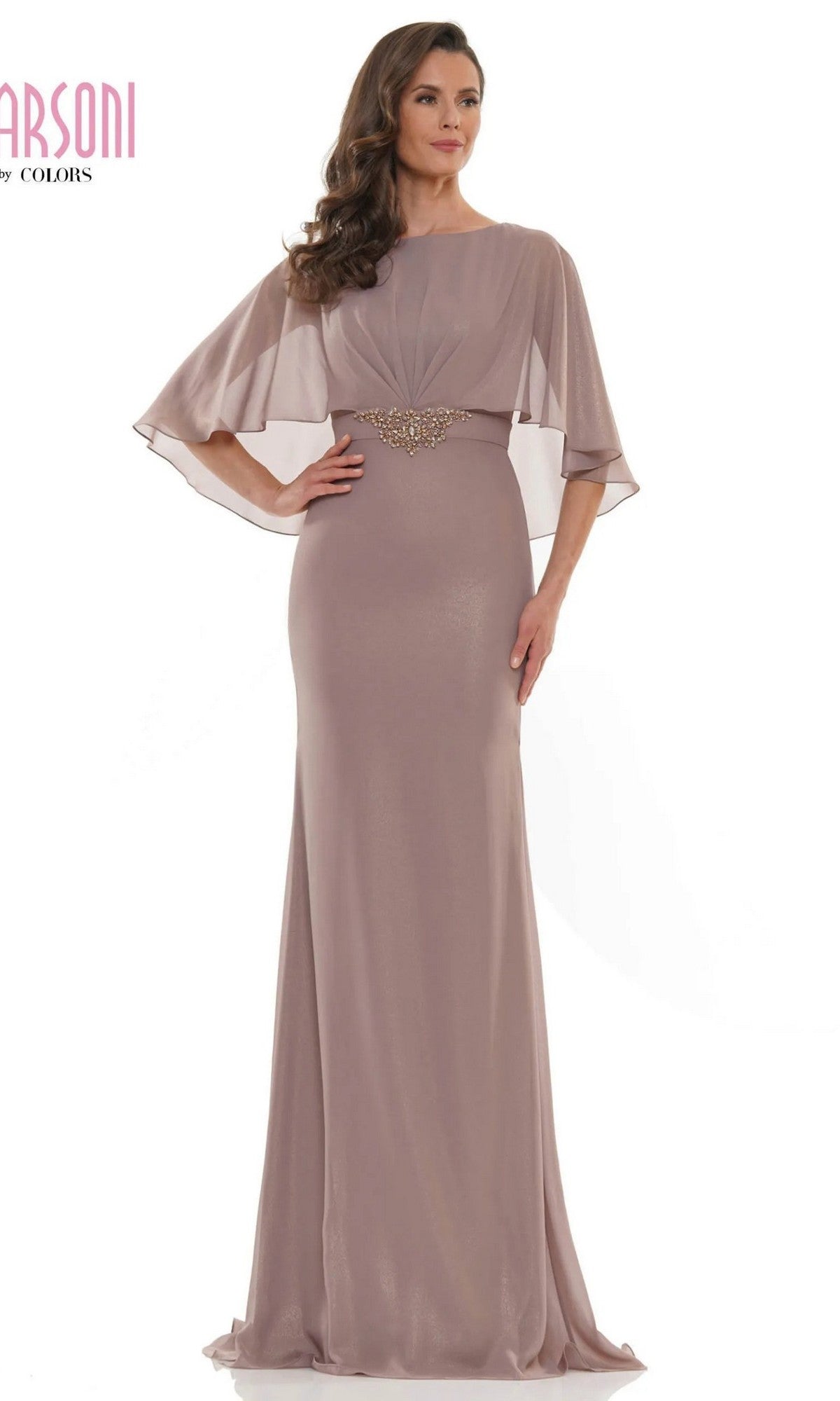 A woman stands in front of a white background wearing the Marsoni MV1130 Long Formal Dress, a modest floor-length taupe sheath with sheer cape sleeves and a decorative waistband.